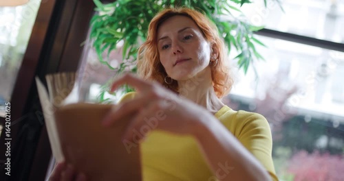 Wallpaper Mural Woman enjoys reading a book at a cafe in Paris on a rainy morning while wearing a yellow shirt and looking at the pages Torontodigital.ca
