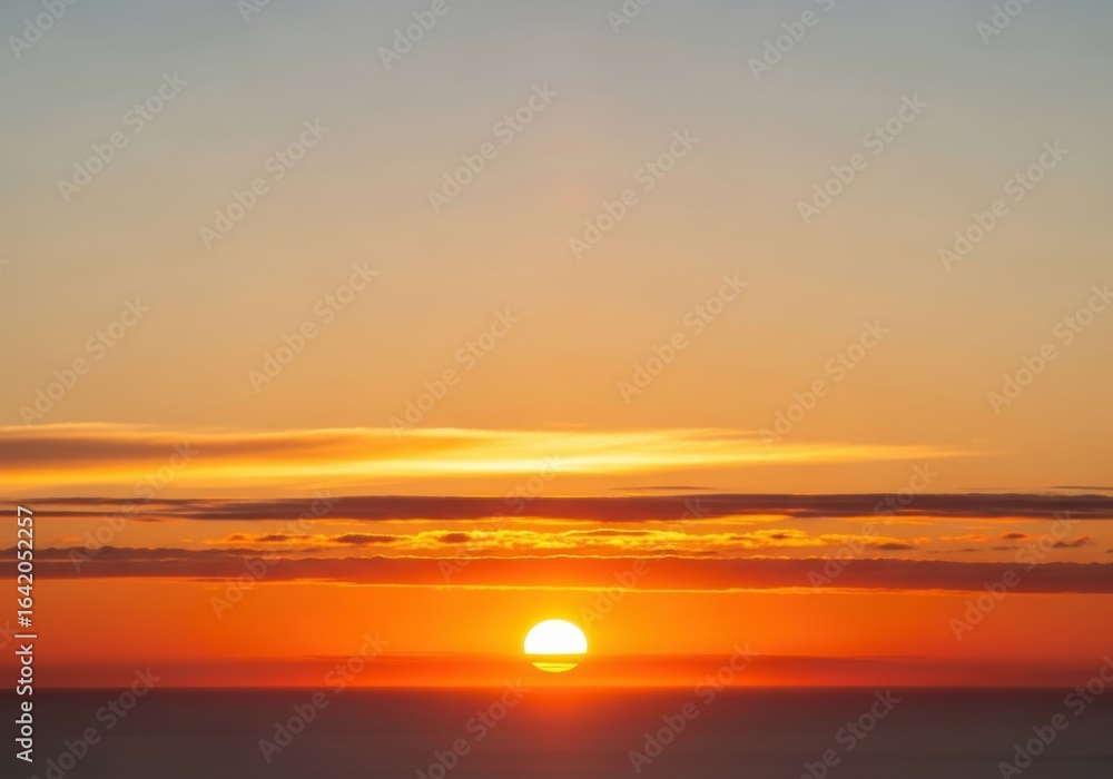 Obraz premium Golden sunset over the calm ocean horizon with vibrant orange and yellow sky and soft clouds