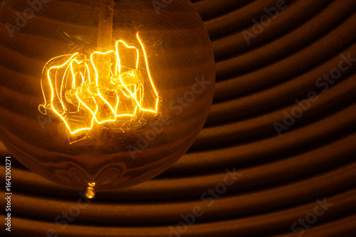 Vintage Light Bulb Filament Close-Up with Glowing Warm Light and Abstract Circular Background.