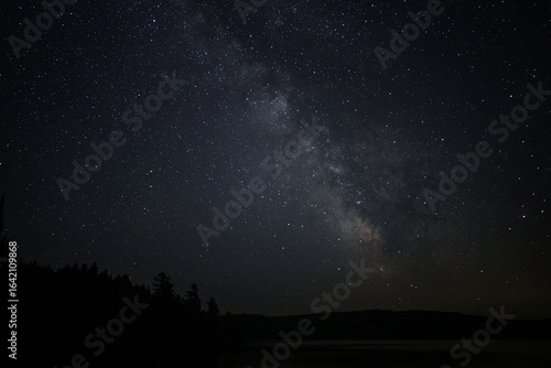 A night scene of a star filled sky and a faint glow of the Milky Way over a calm fresh water lake