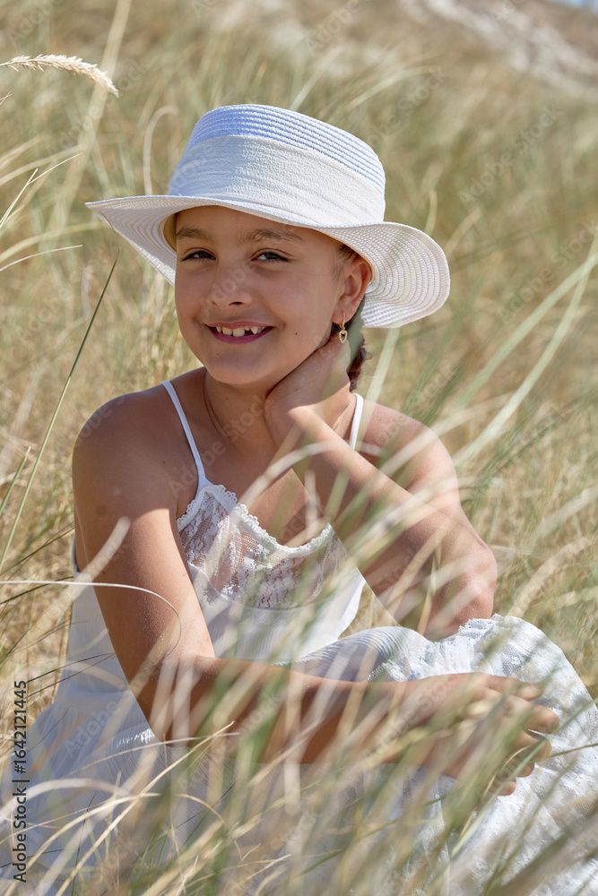 Fototapeta premium Young girl in a white hat enjoying a sunny day in a grassy field