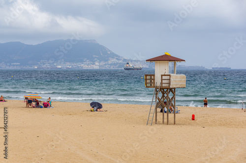 Algeciras Beach, with the lifeguard watchtower on one side, several swimmers, and the Rock of Gibraltar in the background.