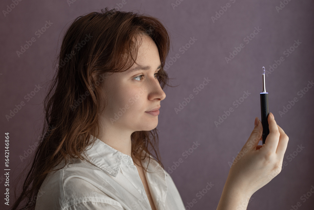 Fototapeta premium Ear Cleaning Technology, woman uses Digital Ear Scope, Earwax Cleaner With Gyroscope, Camera, Light. Cleaning Ears Device Connected to Smartphone