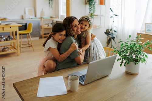 Mother working from home and receiving hugs from daughters