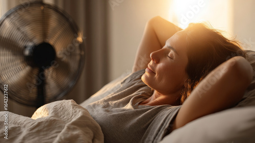 A woman is laying on a bed with a fan in the background