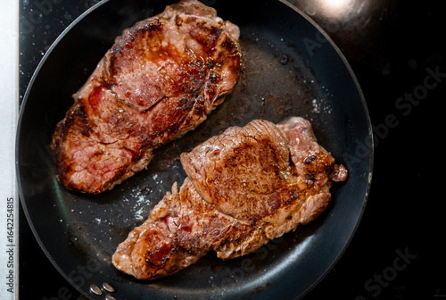 Grilled beef steaks searing in a hot frying pan