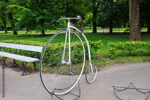 Quadro su tela White vintage bicycle with a large front wheel and a small rear wheel in a city park