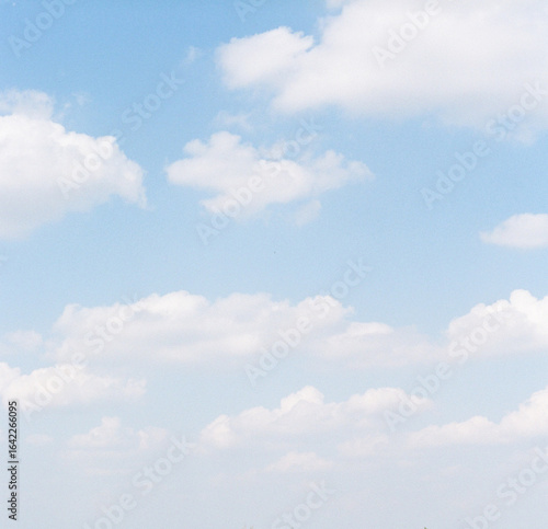 Fluffly white clouds against pale blue sky on film
