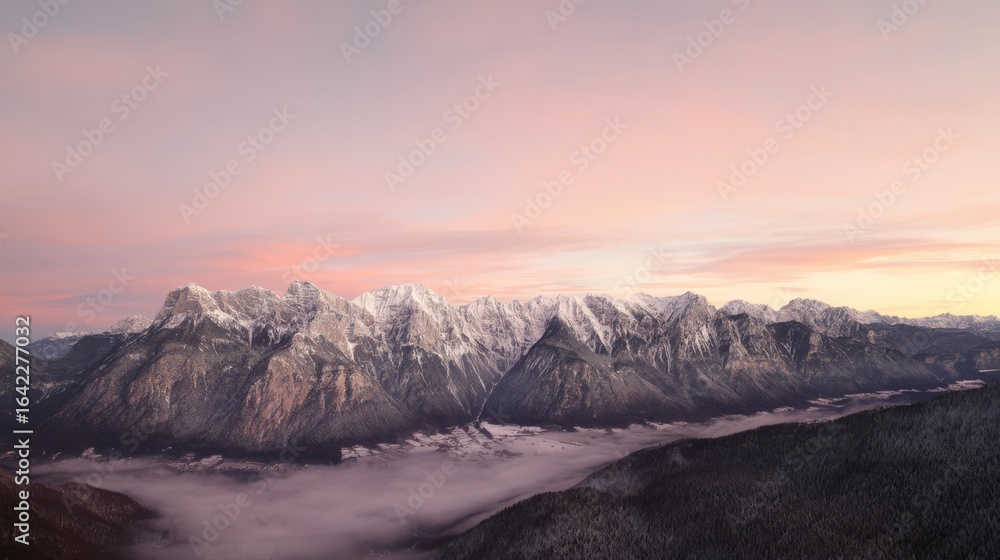 Obraz premium Majestic mountain range at sunrise with soft pink and orange hues over snowy peaks and misty valleys.