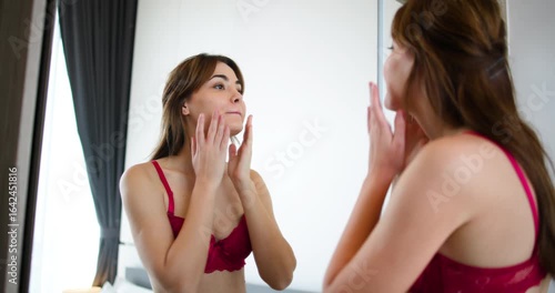 oung woman wearing a red lace lingerie set, standing in front of a mirror and applying lipstick.self-car and modern lifestyle oung woman wearing a red lace lingerie set, standing in front of a mirror 