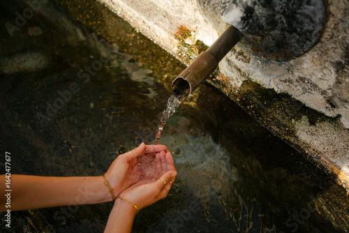 hands of young woman getting spring water at rural fountain 