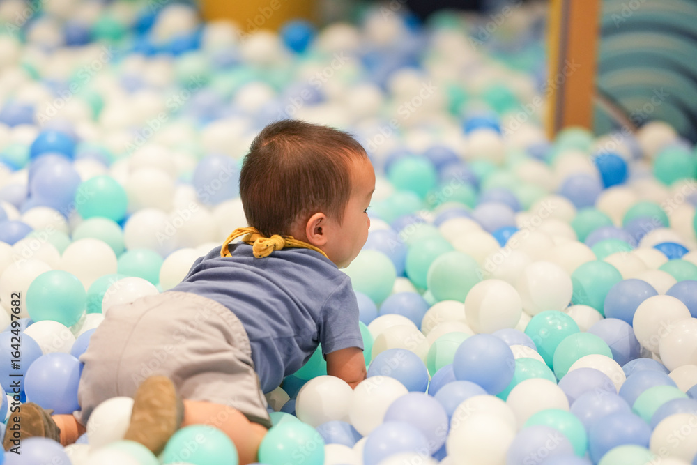 Obraz premium In an indoor play area, a one-year-old Chinese baby plays as if swimming in a pool of plastic balls. Hongkou District, Shanghai, China. Spring.