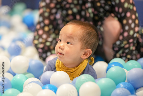 In an indoor play area, a one-year-old Chinese baby and her mother in her thirties play as if swimming in a pool of plastic balls. Hongkou District, Shanghai, China. Spring.