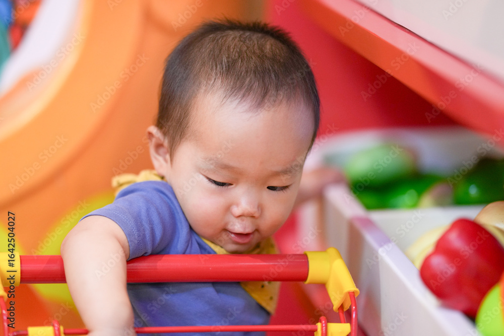 A Chinese baby enjoys shopping with a basket at a supermarket and kitchen style indoor play area. Hongkou District, Shanghai, China. Spring. A Chinese baby enjoys shopping with a basket at a supermarket and kitchen style indoor play area. Hongkou District, Shanghai, China. Spring.