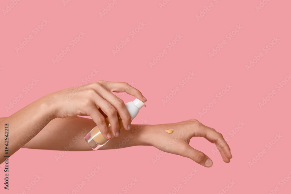 Fototapeta premium Woman applying makeup foundation on pink background