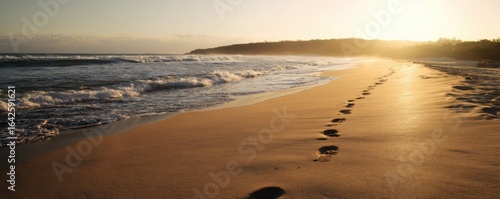 Footprints trace the golden beach as waves gently roll during a vibrant sunrise