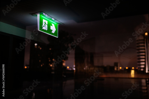 Green exit sign glows in dark, reflecting city lights.