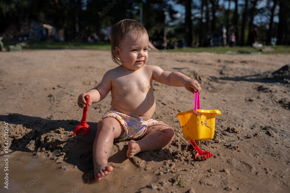 joyful toddler playing with bright plastic toys in a sandy outdoor park, enjoying a sunny day amidst nature, surrounded by trees and distant park-goers, spontaneous, sandcastle, explore, freedom joyful toddler playing with bright plastic toys in a sandy outdoor park, enjoying a sunny day amidst nature, surrounded by trees and distant park-goers, spontaneous, sandcastle, explore, freedom