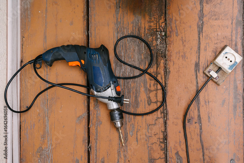 Corded drill on wooden floor next to electrical outlet