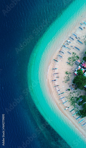 Seaside fishing village with colorful boats and turquoise waves from above.