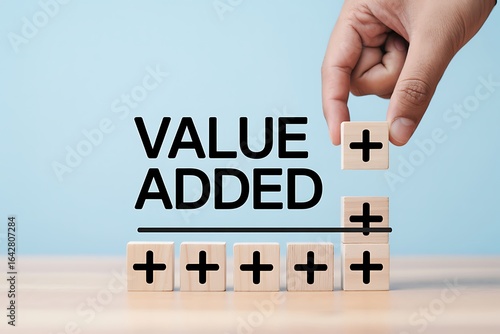 Hand placing a wooden block with a plus sign above the text 'VALUE ADDED,' symbolizing growth, value creation, and the positive impact of contributions.