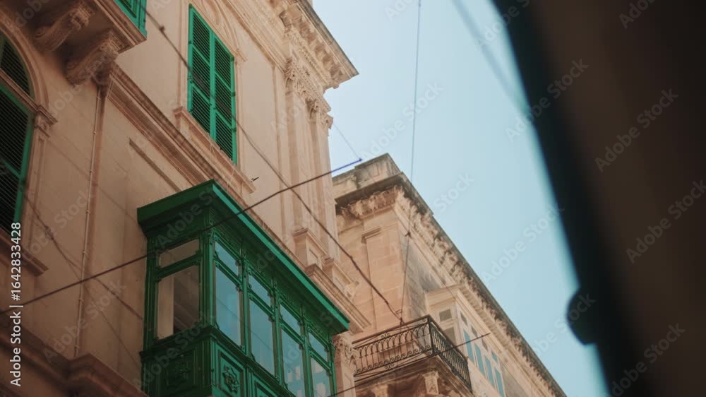 Sunlit Maltese facade with green shutters and a traditional balcony. Warm limestone architecture reflecting the island’s heritage and Mediterranean charm under clear skies. Sunlit Maltese facade with green shutters and a traditional balcony. Warm limestone architecture reflecting the island’s heritage and Mediterranean charm under clear skies.