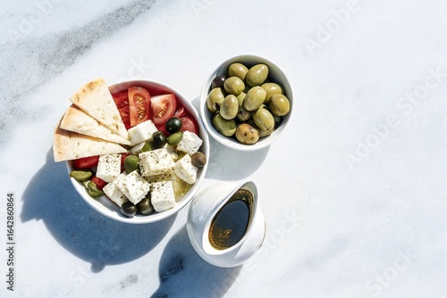 Mediterranean Brunch Set with flat lay of olives, feta cheese, fresh tomato salad, pita bread, and olive oil served on a light stone background