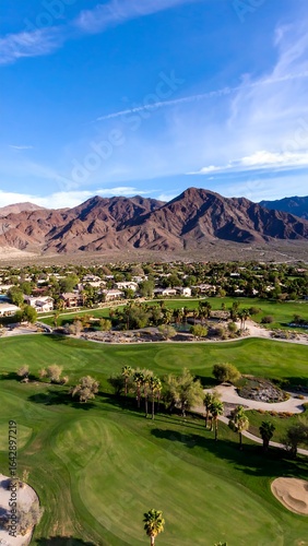 Aerial view of a desert golf course nestled against a mountain range under a clear blue sky