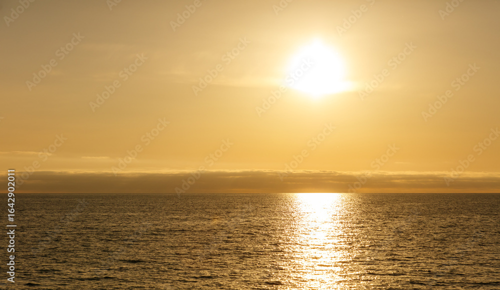 Fototapeta premium The sun is setting over the ocean, casting a warm glow on the water