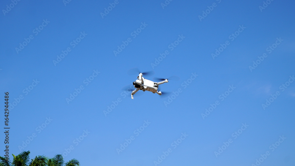 Obraz premium Drone hovering gracefully in mid-air with a clear, bright blue sky, perfect for capturing high-quality aerial images