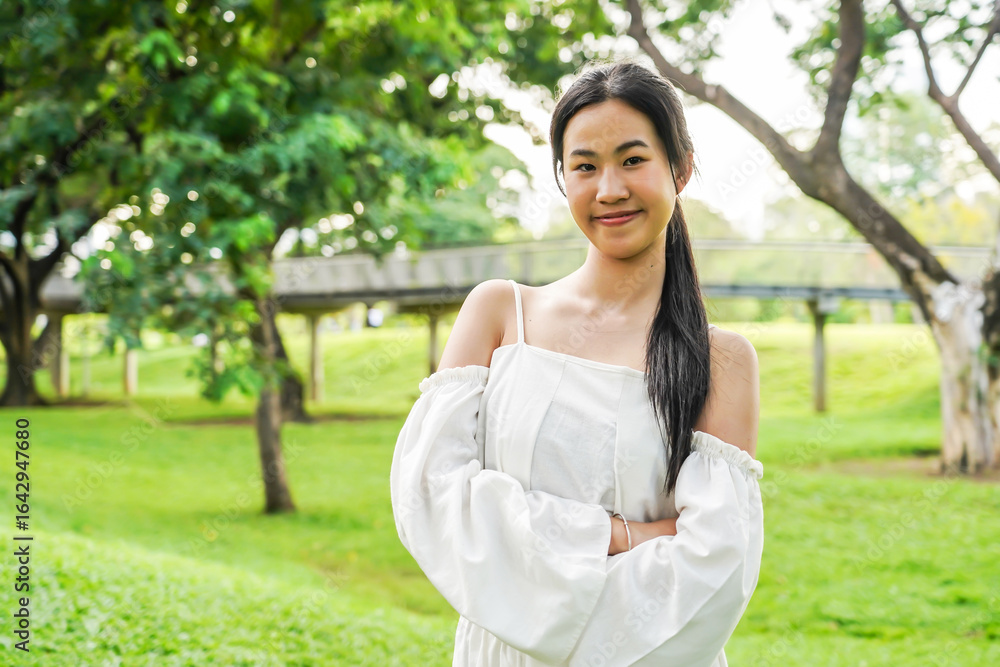 Young asian woman smiling in a sunny outdoor park, surrounded by green trees, enjoying a casual moment in nature, relaxed, with a cheerful expression, peaceful outdoor setting Young asian woman smiling in a sunny outdoor park, surrounded by green trees, enjoying a casual moment in nature, relaxed, with a cheerful expression, peaceful outdoor setting