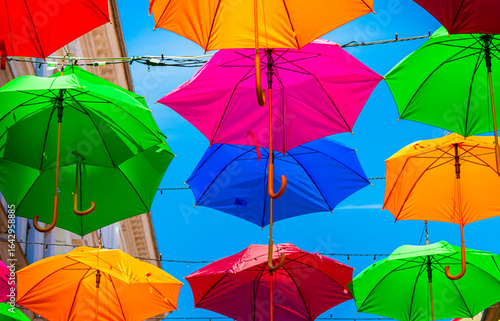 Colorful umbrellas on the blue sky background. Multicolored open umbrellas above a beautiful street as decorations. Hanging rainbow umbrellas over clear blue sky. Abstract color background