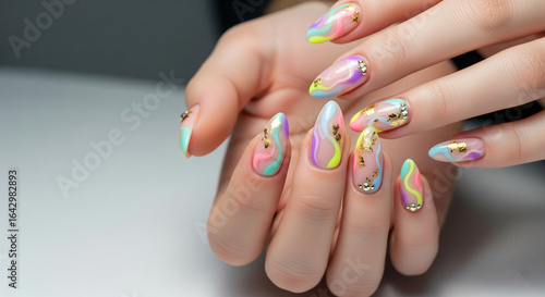 Close-up of hands showcasing long, almond-shaped nails with vibrant abstract rainbow designs, chrome accents, and sparkling rhinestones.