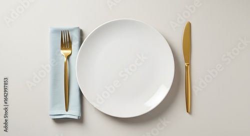 Elegant Table Setting Featuring a Crisp White Plate Gleaming Gold Fork and Knife Accented by a Soft Blue Napkin for a Sophisticated Dining Experience	