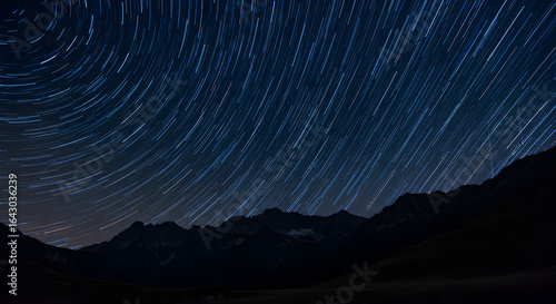 Mesmerizing star trails arc across a dark celestial expanse above majestic mountain silhouettes, capturing the awe of the cosmos