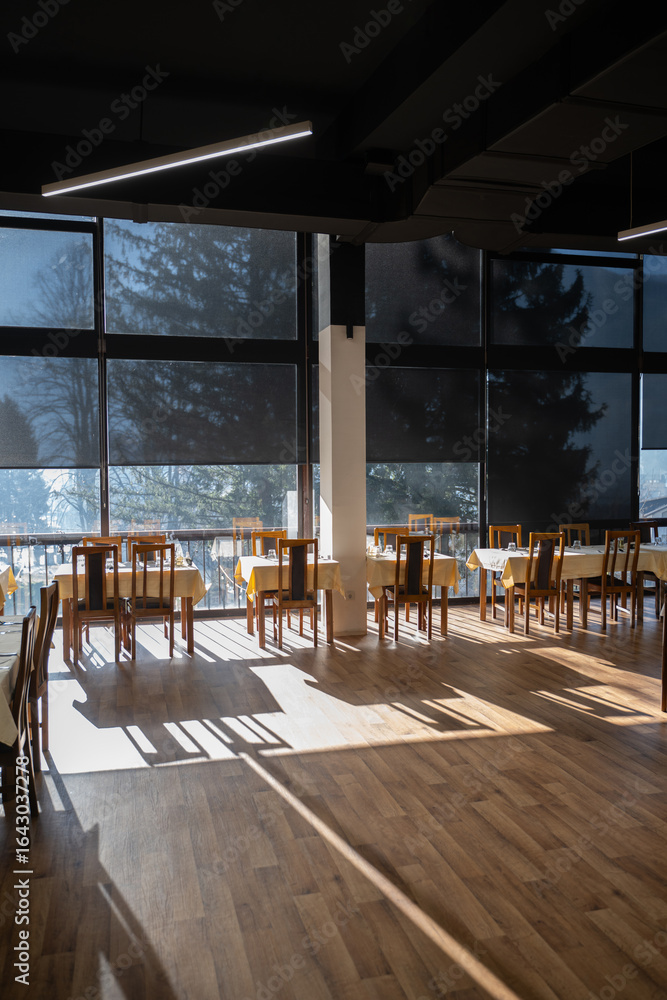 Fototapeta premium Restaurant interior with large sunlit windows and wooden chairs