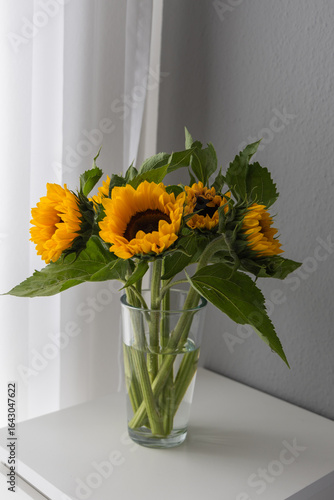 Sunflowers in a glass vase on a white table.