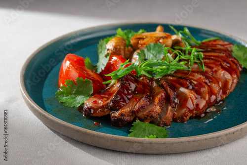 Sliced glazed duck breast served with grilled mushrooms, fresh tomatoes, cilantro and green onions on a rustic blue ceramic plate, Korean fusion presentation