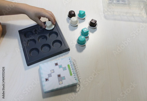 Board game, a visual perception exercise for visual therapy. Pieces of different colors and shapes are placed on the board according to rules. Children's hands playing a board game with pieces.