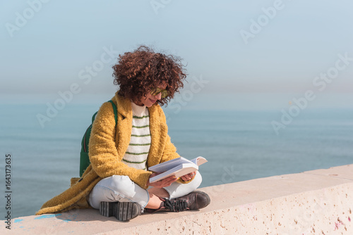 Young woman sitting with cross legs enjoying a relaxing day reading a book by the urban sea