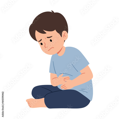 A young boy with a sad face is sitting and holding his stomach, feeling pain from a stomach ache or indigestion.