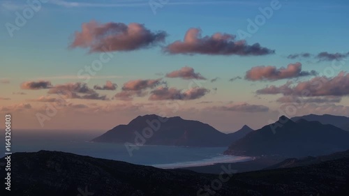 Aerial view of the rugged coastline meeting the silhouetted mountains under a pastel sky with clouds painted in soft pink hues, Cape Town, Western Cape, South Africa.