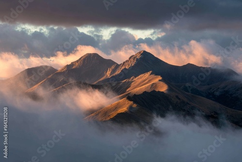 Dramatic mountain range at sunrise with low clouds, mist, and warm light across jagged peaks.