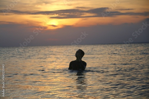 Wallpaper Mural Silhouette of a man sitting in calm sea waters at sunset, perfect for peaceful and travel-themed visuals Torontodigital.ca