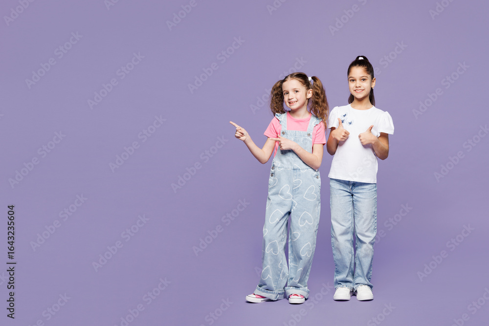 Fototapeta premium Full body fun little two friends kids children girls 9-10 years old wear casual clothes together point index finger aside on area show thumb up isolated on plain purple background. Lifestyle concept.