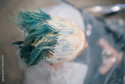A person's head with blue and blonde hair is covered in white hair treatment product. This is a close-up view of a hair dyeing or bleaching process in a salon.