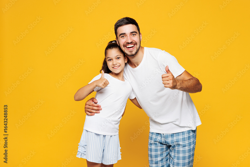 Young parent man have fun with child girl in casual blue pyjamas clothes. Daddy little kid daughter showing thumb up like gesture isolated on plain yellow background. Father's Day Love family concept. Young parent man have fun with child girl in casual blue pyjamas clothes. Daddy little kid daughter showing thumb up like gesture isolated on plain yellow background. Father's Day Love family concept.