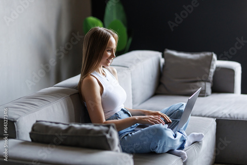 Free Download Young woman hold use work on laptop waving hand talk by video call sit on sofa at home - GFXLoad