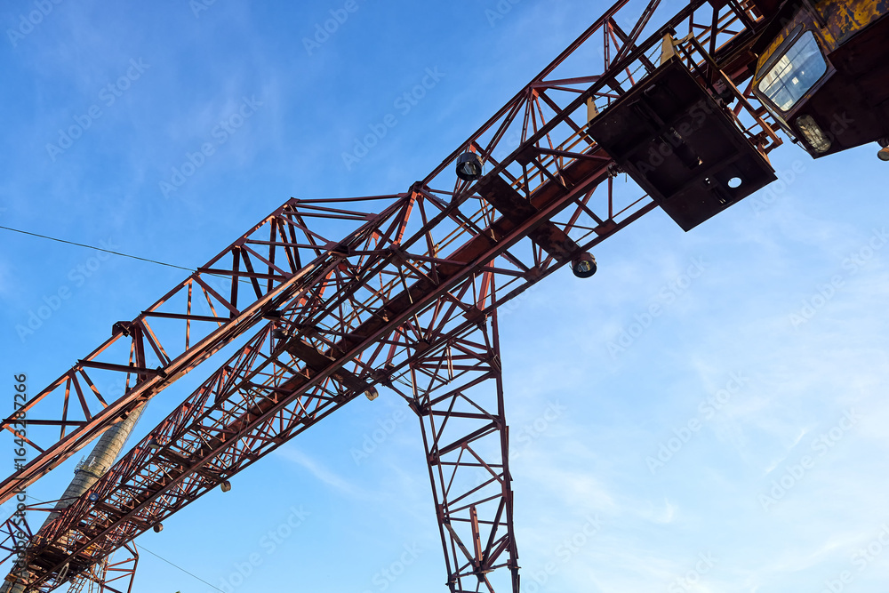 Steel gantry crane structure against blue sky, angular truss design with beams and joints. Used in construction industry, industrial lifting operations, heavy-duty load-bearing applications Steel gantry crane structure against blue sky, angular truss design with beams and joints. Used in construction industry, industrial lifting operations, heavy-duty load-bearing applications