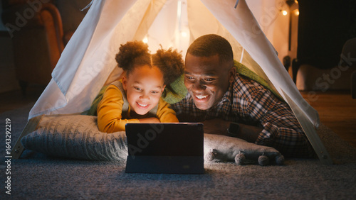 Father And Daughter At Home Lying In Indoor Tent Or Camp Watching Or Streaming To Digital Tablet